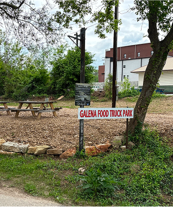 A sign reading "Galena Food Truck Park" stands in a grassy area with picnic tables, surrounded by trees and shrubs. Nearby, you'll find Cabin Rentals and RV Park in Galena MO for a comfortable stay close to the action.